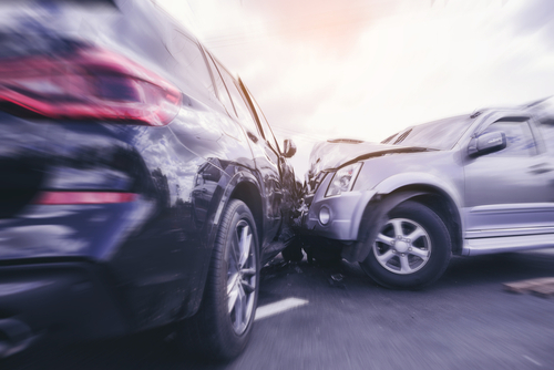 Blurred motion photo of a high-speed car collision showing two vehicles crashed head-on with visible damage to the front of both cars.