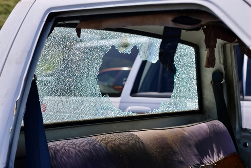 Close-up of a car door with a shattered side window, showing broken safety glass and interior damage after an accident.