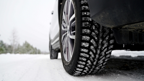 Close-up of a car tire with snow treads driving on a snowy road, showing traction for winter driving.