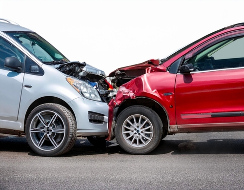 Head-on collision between a silver car and a red car, both with significant front-end damage.