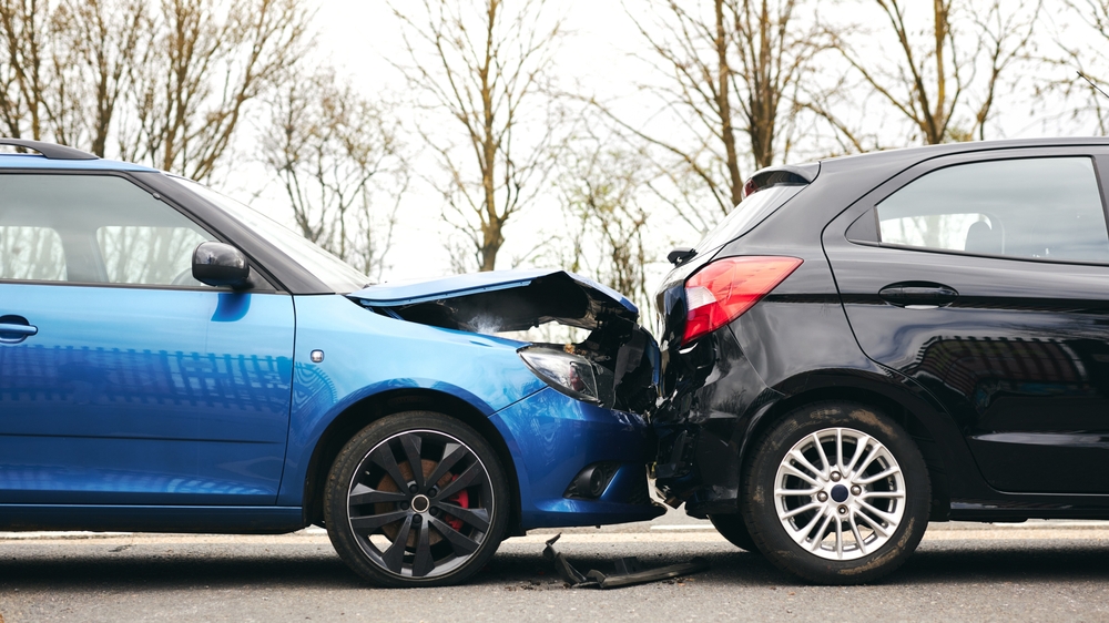 Car accident scene with a blue vehicle crashing into a black car on the road. Concept of traffic collision, insurance, road safety, and vehicle damage.
