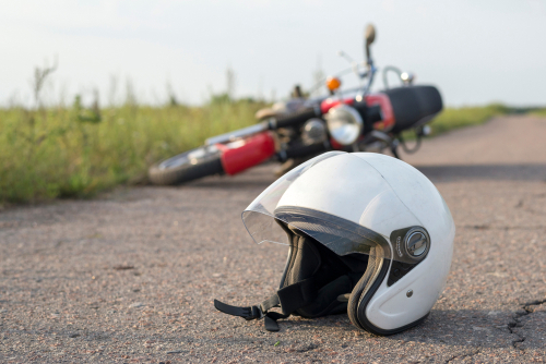 White motorcycle helmet lying on a rural road with a fallen motorcycle in the background.