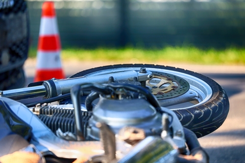 Close-up of a motorcycle wheel lying on its side near an orange traffic cone after an accident.