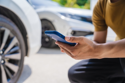 A driver using a smartphone beside a damaged vehicle, representing steps involved in a Washington car accident settlement.