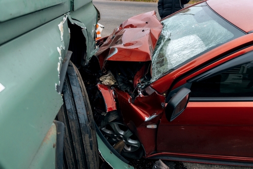 A severely damaged red car crushed into a large truck, illustrating collisions reviewed and pursued by a Seattle truck accident lawyer.